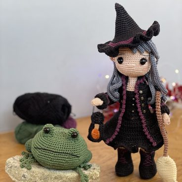 Niona the Halloween Witch, a crocheted witch doll in a pointed hat, beside a crocheted frog